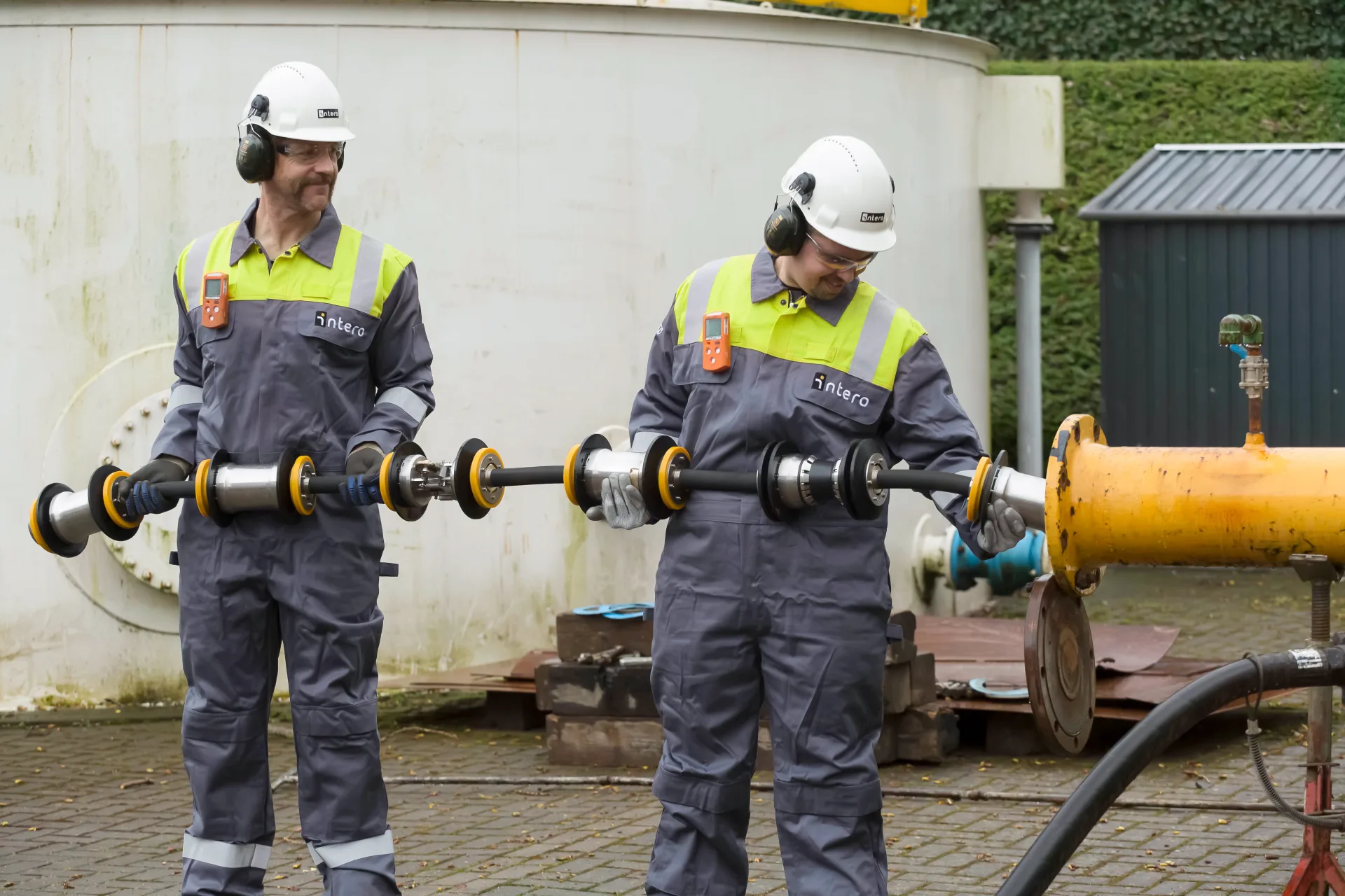 Technicians holding pipeline inspection equipment at an industrial site.